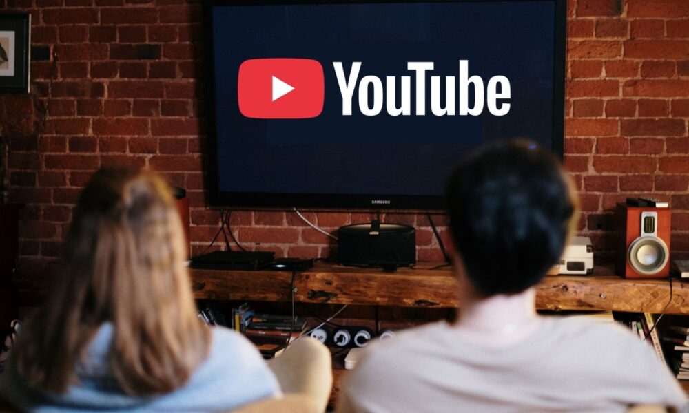Two people look at a television screen with the YouTube logo on it.